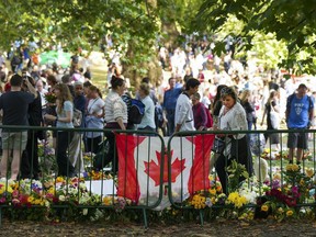Long lines of mourners lay flowers near a Canadian flag as people wait to pay their respects to Queen Elizabeth II near the gates of Buckingham Palace in London on Sunday, Sept. 11, 2022. The British Columbia government says it will follow the federal government's lead and honour the national day of mourning to mark the funeral for the Queen.