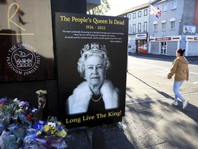 FILE - A woman walks past a picture of Queen Elizabeth II on the Loyalist Shankill Road in west Belfast, Sept. 10, 2022. Britain's longest-reigning monarch and a rock of stability across much of a turbulent century, died Thursday Sept. 8, 2022.