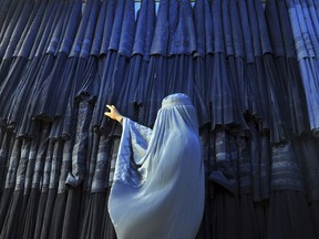 FILE - A woman clad in a burqa looks at other pieces of Afghanistan's traditional, all-encompassing dress at a store in Mazar-i Sharif, north of Kabul, Afghanistan, on Sept. 10, 2015. The Taliban announced they have arrested and will soon sentence an Afghan woman who appeared in a video on social media on Aug. 30, 2022, and said a senior Taliban official forced her into marriage and raped her repeatedly.