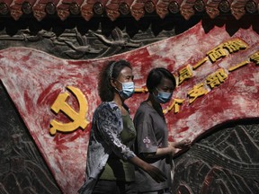 Women wearing face masks walk by a mural depicting a communist party flag and a party slogan in Beijing, Tuesday, Sept. 6, 2022. China has locked down millions of its citizens under tough COVID-19 restrictions and is discouraging domestic travel during upcoming national holidays.