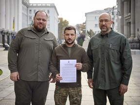In this photo provided by the Ukrainian Presidential Press Office, Ukrainian President Volodymyr Zelenskyy, center, alongside Prime Minister Denys Shmyhal, right, and the head of Verkhovna Rada (Supreme Council of Ukraine) Ruslan Stefanchuk, holds an application for ''accelerated accession to NATO'' in Kyiv, Ukraine, Friday Sept. 30, 2022. (Ukrainian Presidential Press Office via AP)