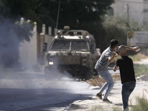A Palestinian throws stones at an Israeli military vehicle following a deadly raid in the occupied West Bank town of Jenin, Wednesday, Sept. 28, 2022. At least four Palestinians were killed and dozens of others wounded, the Palestinian Health Ministry reported, the latest in a series of deadly Israeli operations in the occupied territory.