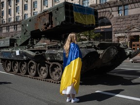 A young woman wrapped in the Ukrainian flag walks next to burnt Russian military vehicles, in Kyiv on Aug. 24.