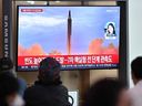 People sit near a television broadcasting a newscast with archival footage of a North Korean missile test, at a train station in Seoul on October 6, 2022.