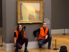 This handout picture released on October 23, 2022 by climate mouvement "Last Generation" shows activists of the group being glued underneath the painting "Les Meules" by French artist Claude Monet after throwing mashed potatoes on the artwork in the Barberini museum in Potsdam on October 23, 2022.