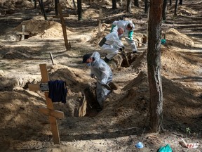 Ukrainian workers exhume bodies from a mass grave in Izium, Ukraine, on Sept. 19.