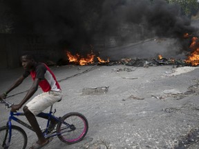 A man rides his bicycle a burning barricade during a protest over the death of journalist Romelo Vilsaint, in Port-au-Prince, Haiti, Sunday, Oct. 30, 2022.