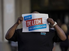 A protester covers his face with a sign mocking city councilmen Kevin de León outside the Los Angeles City Hall in Los Angeles, Tuesday, Oct. 18, 2022. The demonstrators demanded the city council stop its virtual meeting Tuesday until two of its members resign over racist remarks.