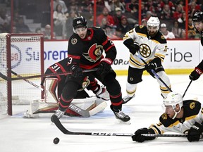 Ottawa Senators defenceman Travis Hamonic (23) tries to get the puck away from Boston Bruins centre Charlie Coyle (13) as he sprawls on the ice during first period NHL hockey action in Ottawa, on Tuesday, Oct. 18, 2022.