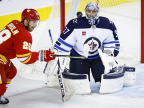 Winnipeg Jets goalie Connor Hellebuyck, right, follows the puck as Calgary Flames forward Elias Lindholm tries to get his stick on it during third period NHL pre-season hockey action in Calgary, Friday, Oct. 7, 2022.THE CANADIAN PRESS/Jeff McIntosh
