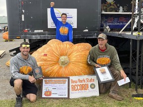 In this photo provided by The Great Pumpkin Farm, Emmett Andrusz, from left, Steve Andrusz and Scott Andrusz, pose with the record setting 2,554-pound pumpkin, in Clarence, N.Y., Saturday, Oct. 1, 2022. Scott Andrusz's entry broke the previous record of 2,528 pounds. (The Great Pumpkin Farm via AP)