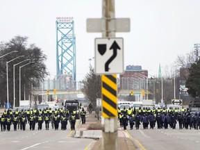 Police walk the line to remove all truckers and supporters after a court injunction gave police the power to enforce the law after protesters blocked the access leading from the Ambassador Bridge, linking Detroit and Windsor, as truckers and their supporters continue to protest against COVID-19 vaccine mandates and restrictions, in Windsor, Ont., Sunday, Feb. 13, 2022.