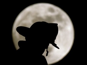 A Lenexa, Kan. firefighter is silhouetted against a full moon as he watches a fire from a ladder truck Monday, May 16, 2011 in Overland Park, Kan. A Quebec workers' health and safety investigation has found that a firefighter who perished in December 2019 blaze near Quebec City when a structure collapsed on him was in the wrong place.THE CANADIAN PRESS/AP-Charlie Riedel
