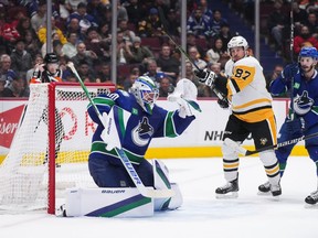 The puck deflects off of Vancouver Canucks goalie Spencer Martin's glove as Pittsburgh Penguins' Sidney Crosby (87) attempts to get his stick on it while Vancouver's Kyle Burroughs, back right, watches during the second period of an NHL hockey game in Vancouver, on Friday, October 28, 2022.