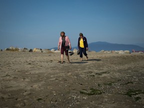 Two women carry their shoes as they walk together at Spanish Banks Beach during a stretch of unseasonably warm weather in Vancouver, B.C., Thursday, Oct. 6, 2022.