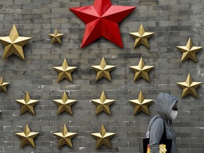 A woman wearing a face mask walks by communist symbol of a stars on display outside a restaurant in Beijing, Sunday, Oct. 9, 2022. Chinese cities are imposing fresh lockdowns and travel restrictions as the number of daily COVID-19 cases tripled during a weeklong holiday and ahead of a major Communist Party meeting in Beijing next week.