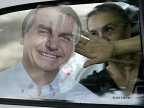 Nara Dauri applies a sticker of Brazil's President Jair Bolsonaro inside a supporter's car window outside a campaign headquarters where voters who support Bolsonaro's campaign for reelection can get campaign swag for free in Campo Grande, Mato Grosso do Sul state, Brazil, Friday, Oct. 21, 2022. The presidential run-off election is set for Oct. 30.