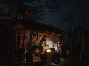 FILE - The Ramos family cooks dinner over a fire outside their storm-damaged home a week after Hurricane Ian knocked out electricity to the entire island, in La Coloma, Pinar del Rio province, Cuba, Oct. 5, 2022. Cuba's energy crisis has once again thrust the Caribbean island into the middle of an escalating tug-of-war between its seaside neighbor, the United States, and ally, Russia. Cuba sees the need to ease U.S. sanctions at the same time that it is benefitting from an influx of Russian oil.