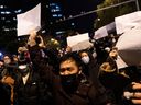 Protesters in Beijing hold sheets of white paper after a vigil for the victims of a fire in Urumqi, China, on Nov. 28, 2022. The ongoing protests in China are about much more than draconian COVID policies, writes Sabrina Maddeaux.