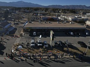 People visit a makeshift tribute with a display of flowers and flags on a corner near the site of a mass shooting at a gay bar Monday, Nov. 21, 2022, in Colorado Springs, Colo.