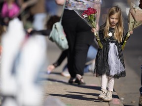 Six-year-old Harper Halvorson carries bouquets of flowers to place a makeshift memorial for victims of a weekend mass shooting at a nearby gay nightclub on Tuesday, Nov. 22, 2022, in Colorado Springs, Colo. Anderson Lee Aldrich opened fire at Club Q, in which five people were killed and others suffered gunshot wounds before patrons tackled and beat the suspect into submission.