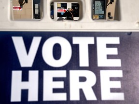 A woman is seen through a "vote here" sign, as she enters a polling site to vote in the midterm elections, Tuesday, Nov. 8, 2022, in Washington.