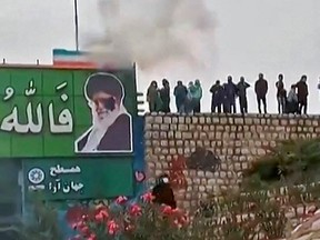 This image grab from a UGC video posted on November 3, 2022, reportedly shows protesters throwing a small explosive device at a banner depicting the Islamic Republic's Supreme Leader Ayatollah Ali Khamenei, as a large crowd enters the district of Fuladshahr near the central city of Isfahan.