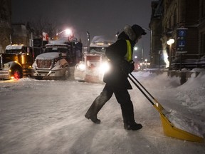 A protester shovels snow from Wellington Street in front of a blockade of trucks as a winter storm warning is in effect, on the 22nd day of a protest against COVID-19 measures that has grown into a broader anti-government protest, in Ottawa, on Friday, Feb. 18, 2022. The commission investigating the federal government's invocation of the Emergencies Act says most of the millions of dollars raised by the "Freedom Convoy" ended up in an escrow account or returned to donors.