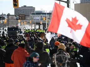 Protesters face police officers on foot and horseback and an armoured vehicle on Colonel By Drive near the truck blockade in Ottawa, on Friday, Feb. 18, 2022.
