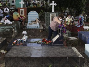 A woman places flowers at the tomb of her relative, next to one of the graves of a gang member whose tombstone was destroyed on the order of the government, during the Day of the Dead at the Nueva San Salvador Cemetery, in Santa Tecla, El Salvador, Wednesday, Nov. 2, 2022. Santa Tecla Mayor Henry Flores said the crews had destroyed nearly 80 tombstones in the municipal cemetery and erased gang-related graffiti.