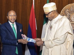 In this photo released by the Nigeria State House, Nigeria's central bank governor, Godwin Emefile, left, presents the newly designed currency notes to Nigeria's President Muhammadu Buhari, right, during a launch in Abuja, Nigeria, Tuesday, Nov. 22, 2022. Nigeria has unveiled newly designed currency notes that the West African nation's central bank says will help curb inflation and money laundering.
