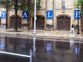 FILE - A woman walks by a Yale sign reflected in the rainwater in the street on the Yale University campus in New Haven, Conn., Aug. 22, 2021. Yale University is being accused in a federal lawsuit filed Wednesday, Nov. 30, 2022, of discriminating against students with mental health disabilities, including pressuring some to withdraw from the prestigious institution and then placing "unreasonable burdens" on those who seek to be reinstated.