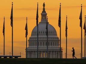 An early morning pedestrian is silhouetted against sunrise as he walks through the U.S. Flags on the National Mall and past the U.S. Capitol Building in Washington, Monday, Nov. 7, 2022, one day before the midterm election will determine the control of the U.S. Congress.