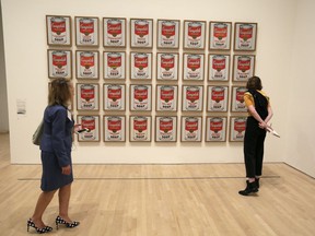 FILE- A pair of women look at the 1962 pop piece called "Campbell's Soup Cans" at the exhibition, "Andy Warhol _ From A to B and Back Again, in San Francisco on May 15, 2019. Climate protesters in Australia on Wednesday, Nov. 9, 2022 scrawled graffiti and glued themselves to an Andy Warhol artwork depicting Campbell's soup cans but didn't appear to damage the piece because it's encased in glass.