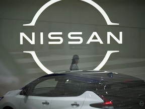 FILE - A staff walking near a Nissan logo at Nissan headquarters is seen though a window on May 12, 2022, in Yokohama near Tokyo. Nissan's profit fell 68% in the last quarter as a shortage of computer chips hindered the Japanese automaker's ability to deliver vehicles to its customers.