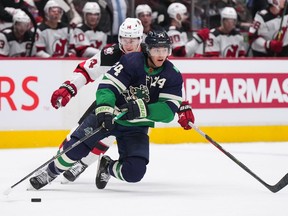 Vancouver Canucks' Ethan Bear (74) skates with the puck in front of New Jersey Devils' Nathan Bastian (14) during the second period of an NHL hockey game in Vancouver, B.C., Tuesday, Nov. 1, 2022.