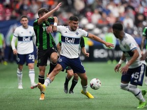 Vancouver Whitecaps' Lucas Cavallini, centre, and Austin FC's Jon Gallagher vie for the ball during the second half of an MLS soccer game in Vancouver, on Saturday, October 1, 2022.