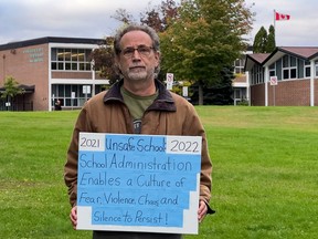 Teacher Michael Sternberg stands outside Pinecrest Public School with a homemade sign in September 2022.