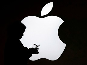A woman looks at a cellphone while standing in front of an Apple logo.
