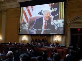 Members of the U.S. House Select Committee investigating the January 6 Attack on the U.S. Capitol sit beneath an image showing former President Donald Trump speaking on the telephone in the Oval Office, during the panel's final meeting on December 19, 2022.