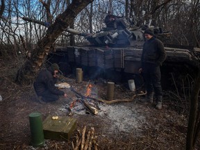 Ukrainian servicemen warm themselves next to their tank