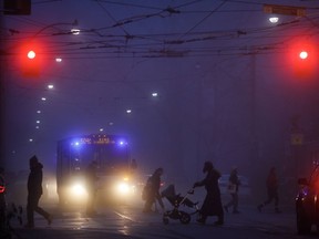 People walk through the headlights of vehicles in the evening fog in Toronto, Thursday, Nov. 24, 2022. A new analysis shows Canada has been gradually closing the gap with the United States when it comes to attracting and keeping new permanent residents.