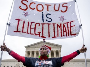 Nadine Seiler of Waldorf, Md., holds a sign that reads "SCOTUS is Illegitimate" in front of the Supreme Court in Washington, Wednesday, Dec. 7, 2022, as the Court hears arguments on a new elections case that could dramatically alter voting in 2024 and beyond. The case is from highly competitive North Carolina, where Republican efforts to draw congressional districts heavily in their favor were blocked by a Democratic majority on the state Supreme Court.