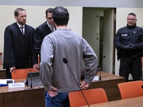 The defendant, front, stands together with his lawyers Martin Gelbricht, rear left, and Maximilian Baer, rear second left, in the courtroom in Munich, Germany, Friday, Dec. 23, 2022. The German court convicted the man of attempted murder and bodily harm and sentenced him to 14 years in prison on Friday over a knife attack on a train last year that left four people wounded.