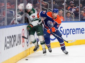 Minnesota Wild's Joel Eriksson Ek (14) is checked by Edmonton Oilers' Connor McDavid (97) during first period NHL action in Edmonton on Friday, December 9, 2022.THE CANADIAN PRESS/Jason Franson