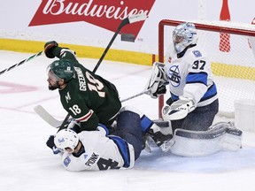 Minnesota Wild's Jordan Greenway (18) and Winnipeg Jets' Neal Poink (4) collide in front of goaltender Connor Hellebuyck (37) during first period NHL action in Winnipeg on Tuesday Dec. 27, 2022.