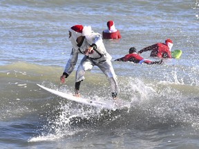 Surfer Corey Howell in a space man Surfing Santa suit, rides with waves with other surfing Santas for the 14th annual Surfing Santas of Cocoa Beach event Christmas Eve morning, Saturday, Dec. 24, 2022. Cold temperatures in the 30s Fahrenheit thinned out the surfers, but thousands showed up for the annual holiday event that benefits the Florida Surf Museum and Grind for Life, a local charity benefiting people with cancer.