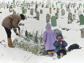 FILE - Fatima Ramic, with her daughter Alma, right and niece Elma, back to camera, tends to the grave of her 8-year-old son, Alija, who died the previous year from medical complications in Sarajevo's Kosevo hospital on Jan. 5, 1995. The mother says her son is a victim of the war due to inadequate facilities and medicines available to the sick and injured of the Bosnian capital.