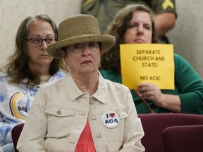 FILE - A woman wearing a button supporting charter schools linked to Hillsdale College sits in front of a woman holding a sign opposing the schools during a meeting of the Tennessee Public Charter School Commission staff on Sept. 14, 2022, in Murfreesboro, Tenn. A contentious charter school operator linked to a conservative Michigan college is taking another swing at opening schools in three Tennessee counties that have previously rejected it, as well as in two new counties.