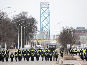 Police walk the line to remove truckers and supporters after a court injunction gave police the power to enforce the law after protesters blocked the access leading from the Ambassador Bridge in Windsor, Ont., Sunday, Feb. 13, 2022. The federal government is giving Windsor up to $6.9 million in compensation for dealing with "Freedom Convoy" protests that blocked the Ambassador Bridge in the southwest Ontario city earlier this year.